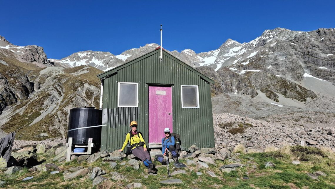 Two trampers at the door of a mountain hut.