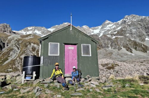 Two trampers at the door of a mountain hut.